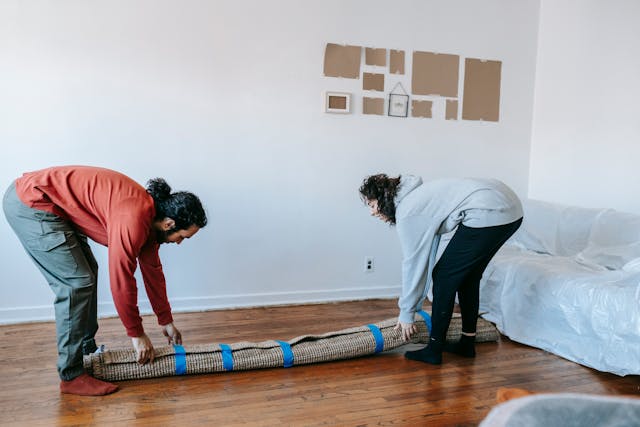 Two people lifting a rolled up carpet